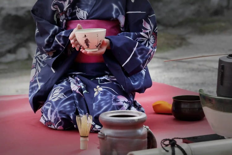 A kimono-clad woman offering hospitality by presenting the bowl with its design facing the guest