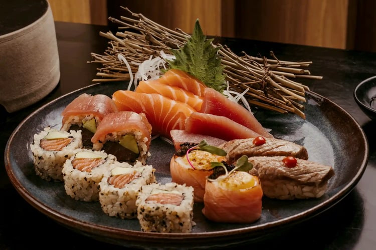 A plate of sushi and chopsticks on a table, with salmon. Kobe