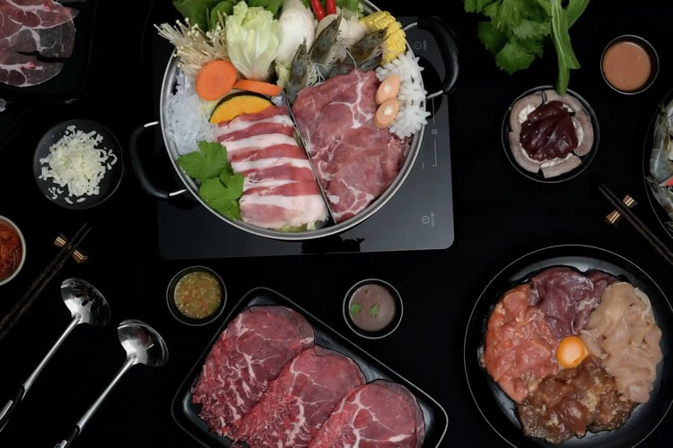 Overhead shot of a shabu-shabu hot pot with fresh, thinly sliced meat, seafood, and vegetables. Dipping sauces are on a black background. Japanese cuisine, Kobe