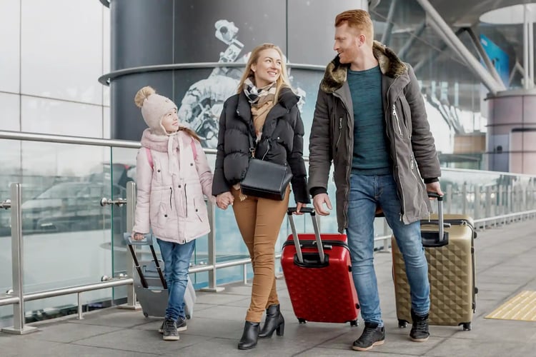 A family walking outside an airport, pulling their carry-on bags