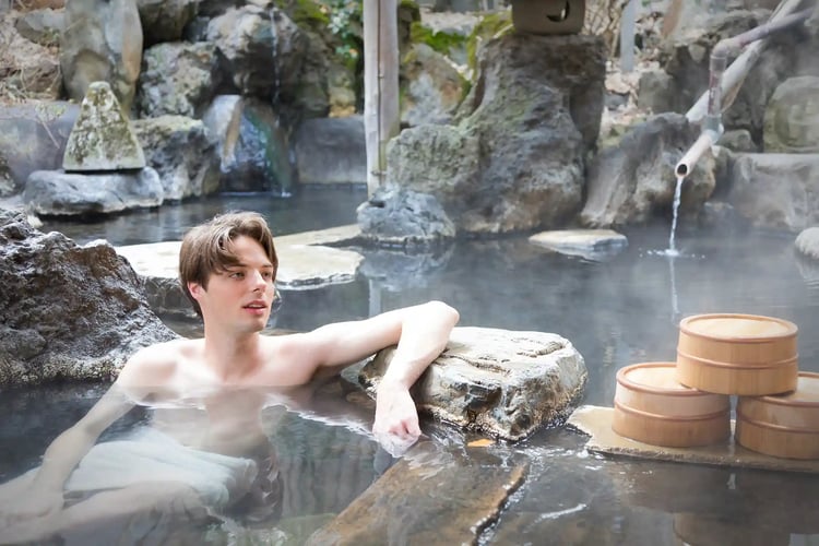 To relax by leisurely soaking in an open-air bath (rotenburo)