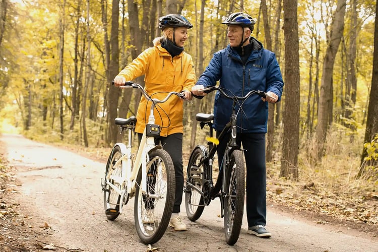 A senior couple walking and pushing bicycles through an autumn forest