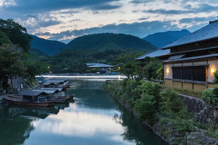 Katsura_River_bank_with_pleasure_boats_and_illuminated_building_at_sunset_Kyoto_Japan