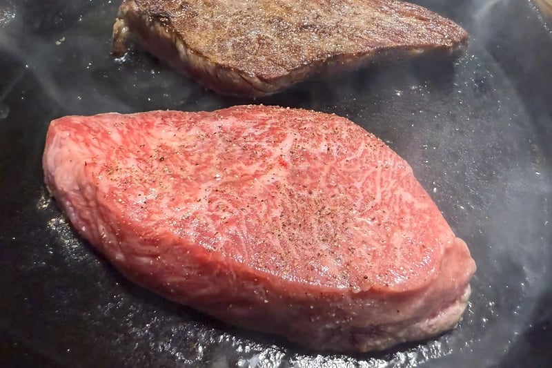 A beef steak searing on a grill