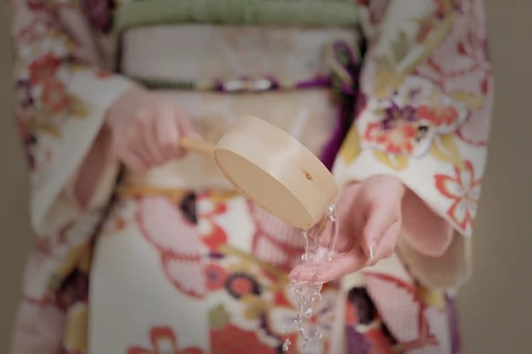 A woman in a kimono performing purification at the Chozuya