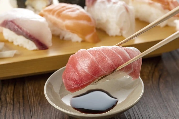 A Close-Up of a Hand Lightly Dipping Sushi into Soy Sauce