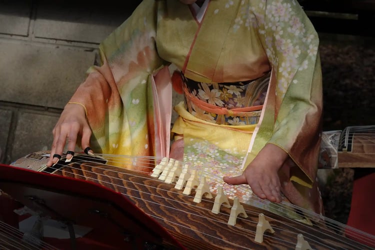 A woman wearing a kimono, strumming the koto