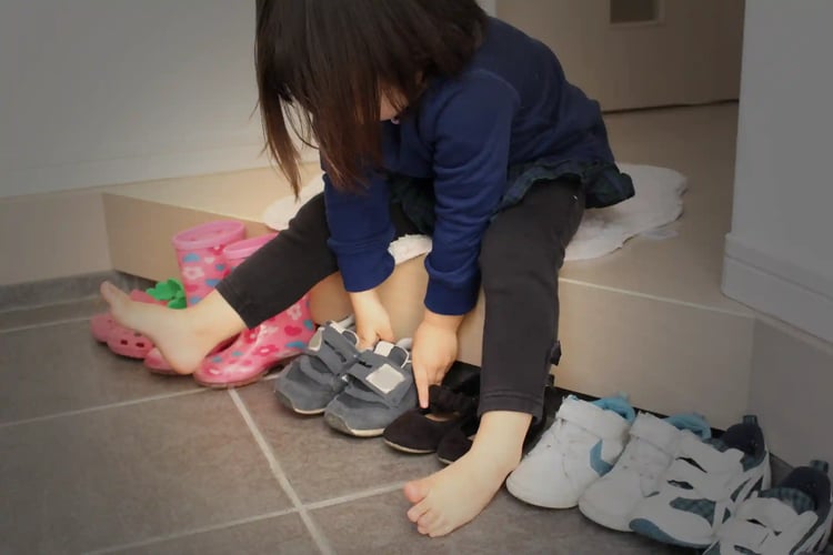 A girl taking off her shoes and neatly lining them up at the entrance