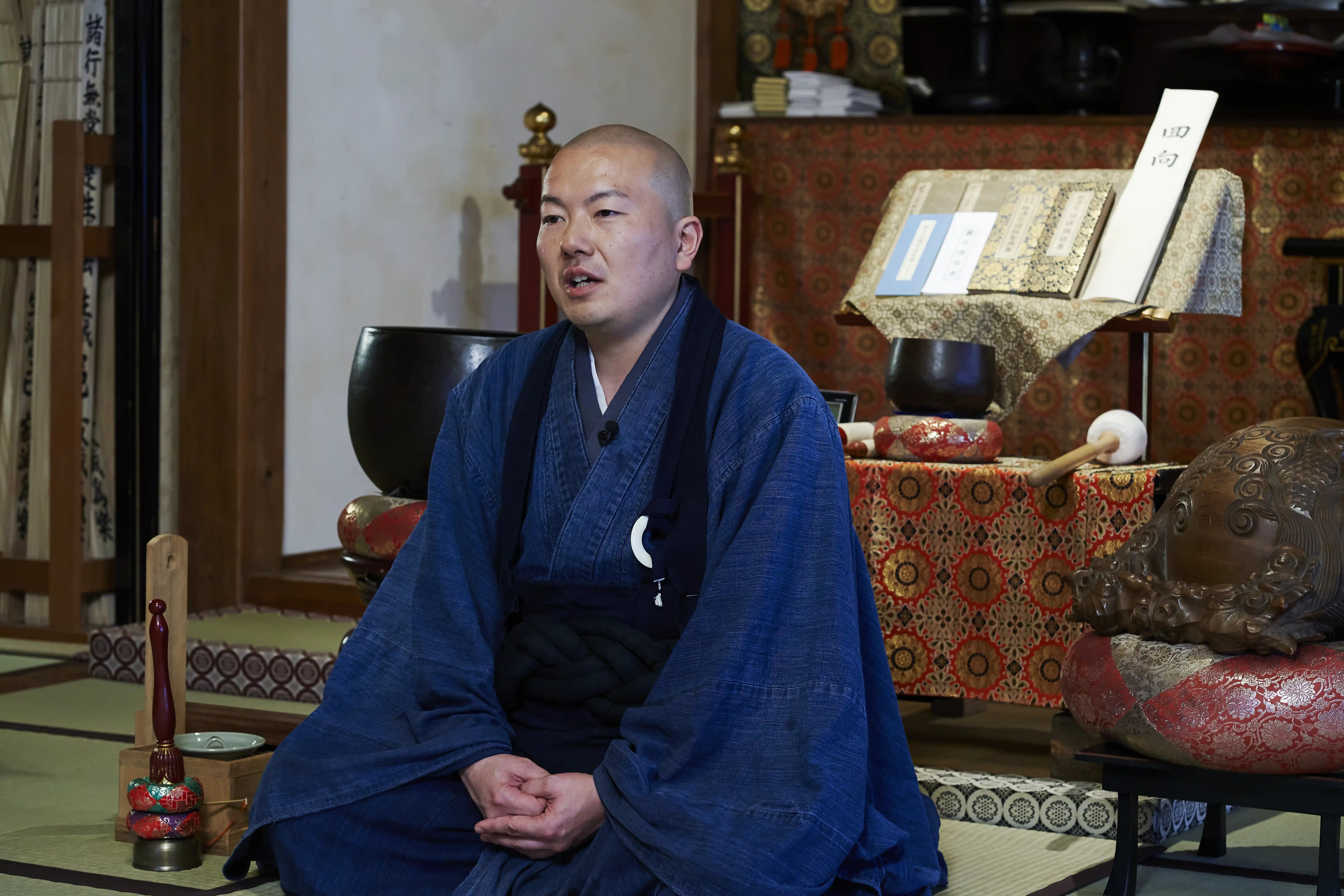 Rev. Taijun Namiki, head priest of Kinryuji, seated on tatami in the temple's main hall beside a large bowl-shaped bell, with light from shoji windows