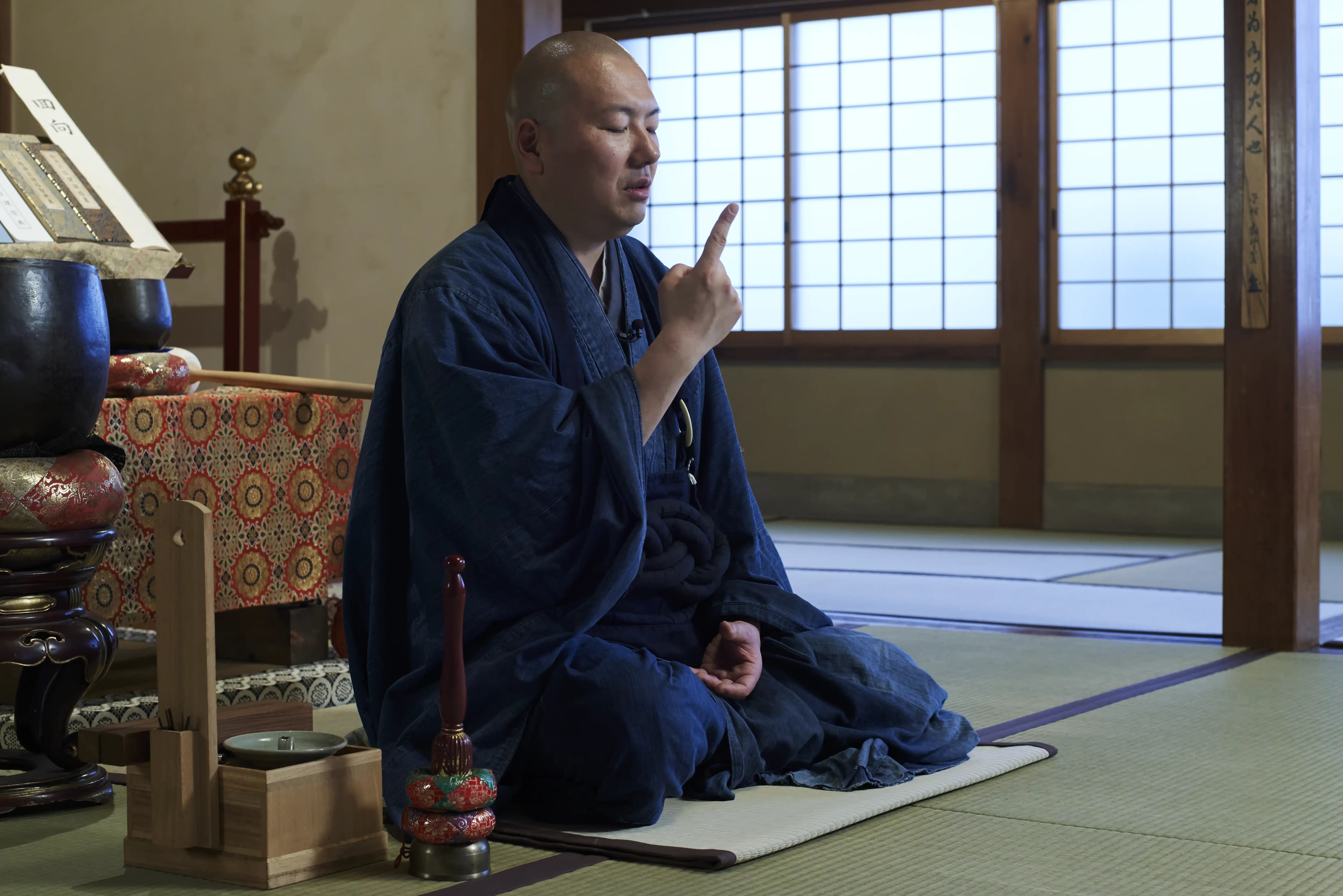 Rev. Taijun Namiki seated on a mat on the tatami of Kinryuji's main hall, eyes lowered and one finger raised as he explains seated practice