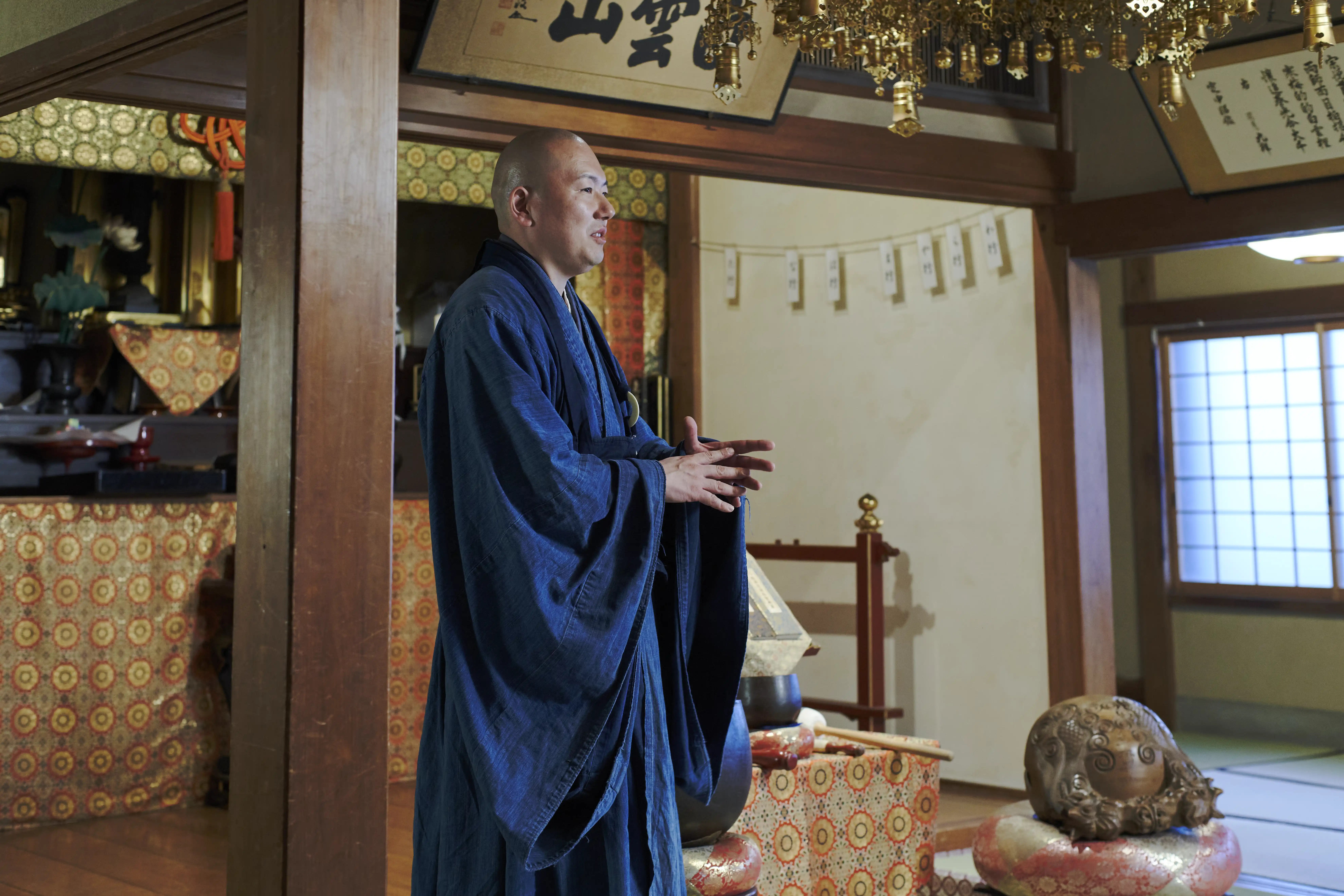 Rev. Taijun Namiki standing in the wooden main hall of Kinryuji, gesturing as he talks