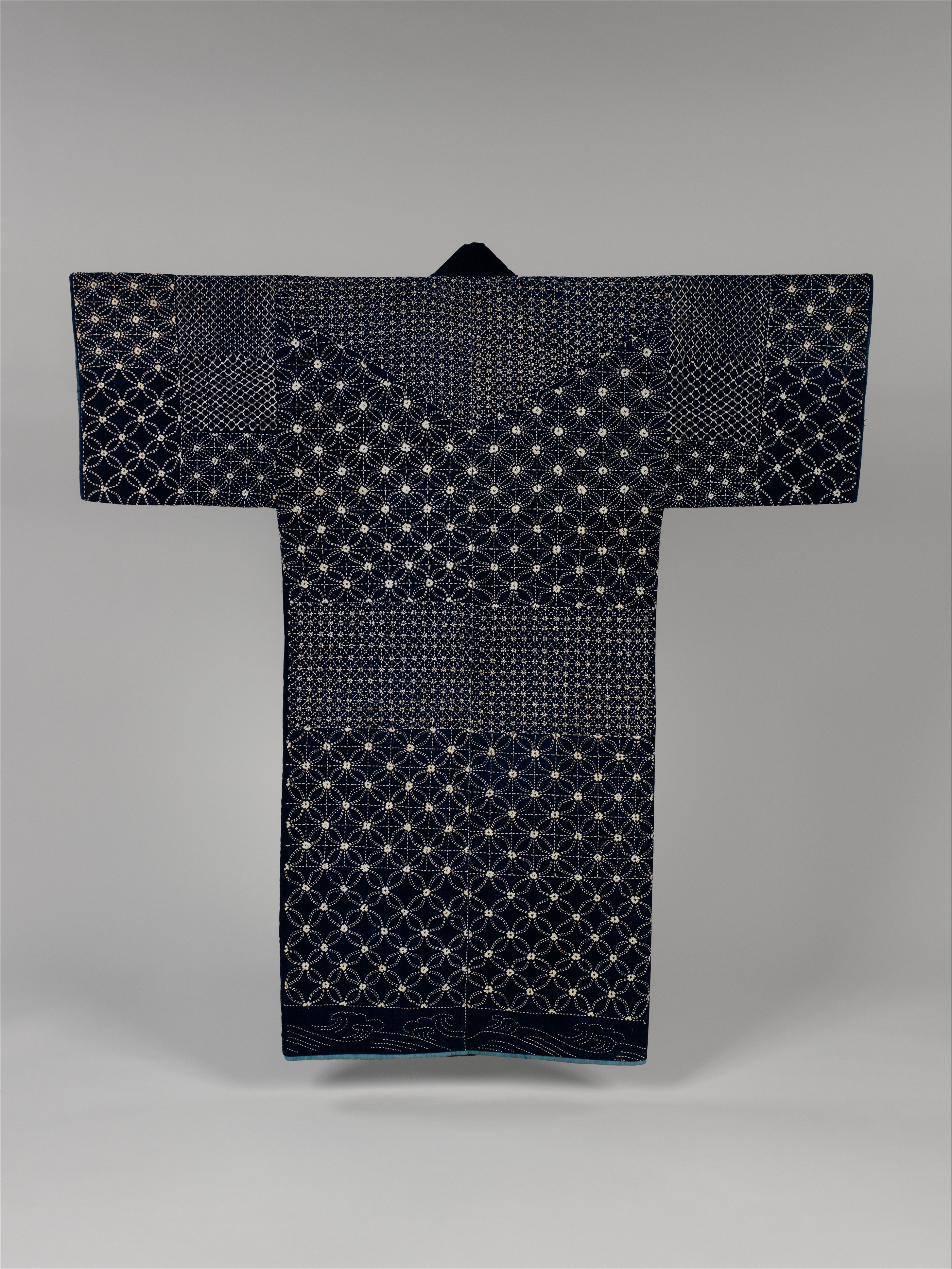 A nineteenth-century sashiko jacket in the Metropolitan Museum of Art, indigo-dyed cotton quilted and embroidered all over in fine white geometric stitching, with a band of waves at the hem