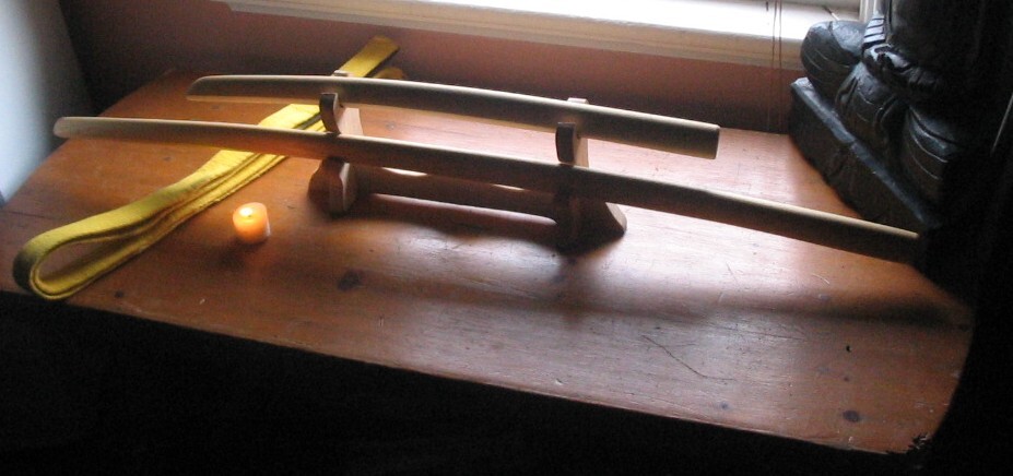 A pair of wooden practice swords, long and short, resting on a stand beside a yellow belt