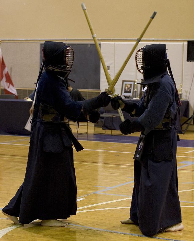 Two kendo practitioners in full bogu armor crossing shinai (bamboo swords) at the start of a bout
