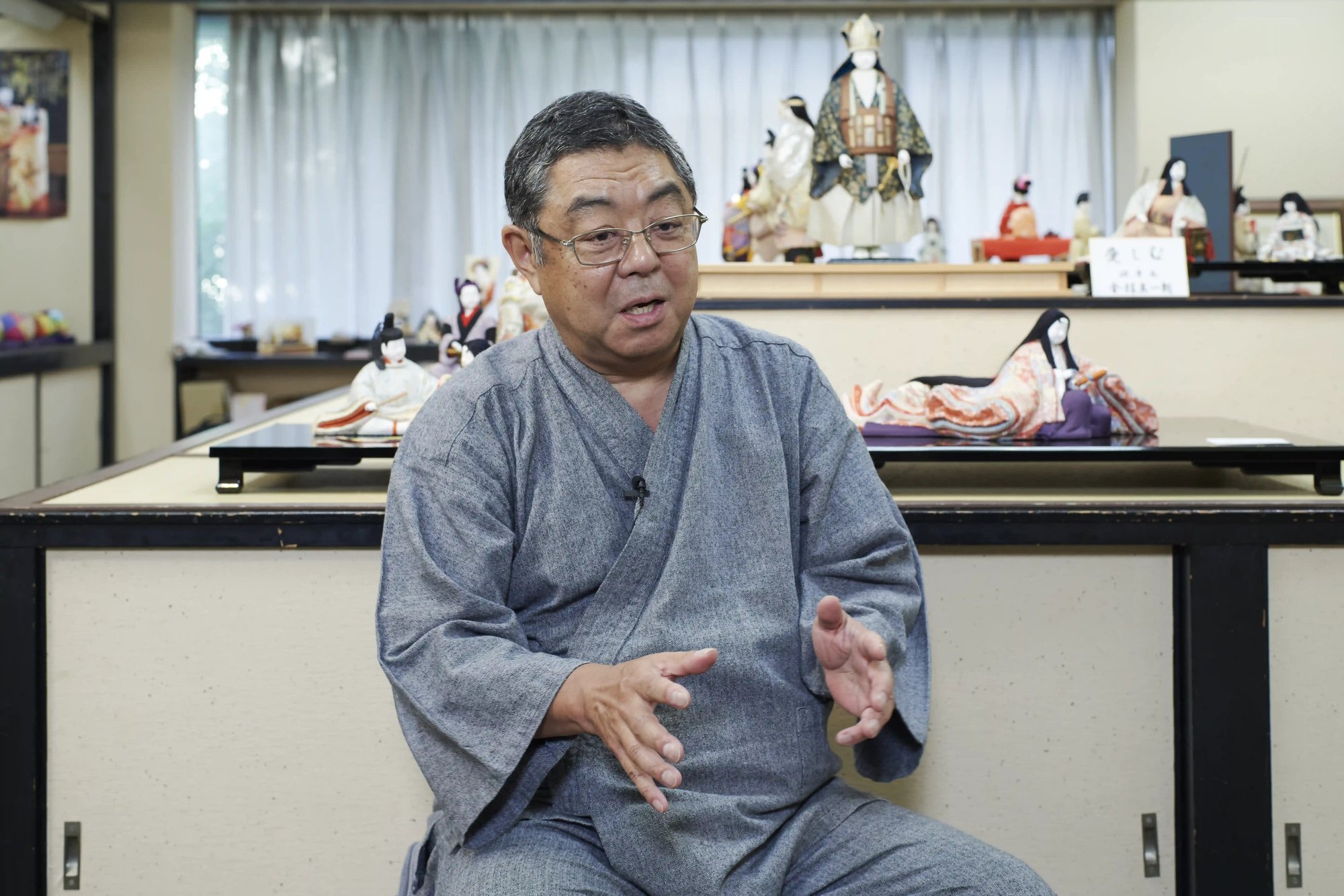 Kenji Kanabayashi speaking in the Mataro showroom, with hina dolls on display behind him