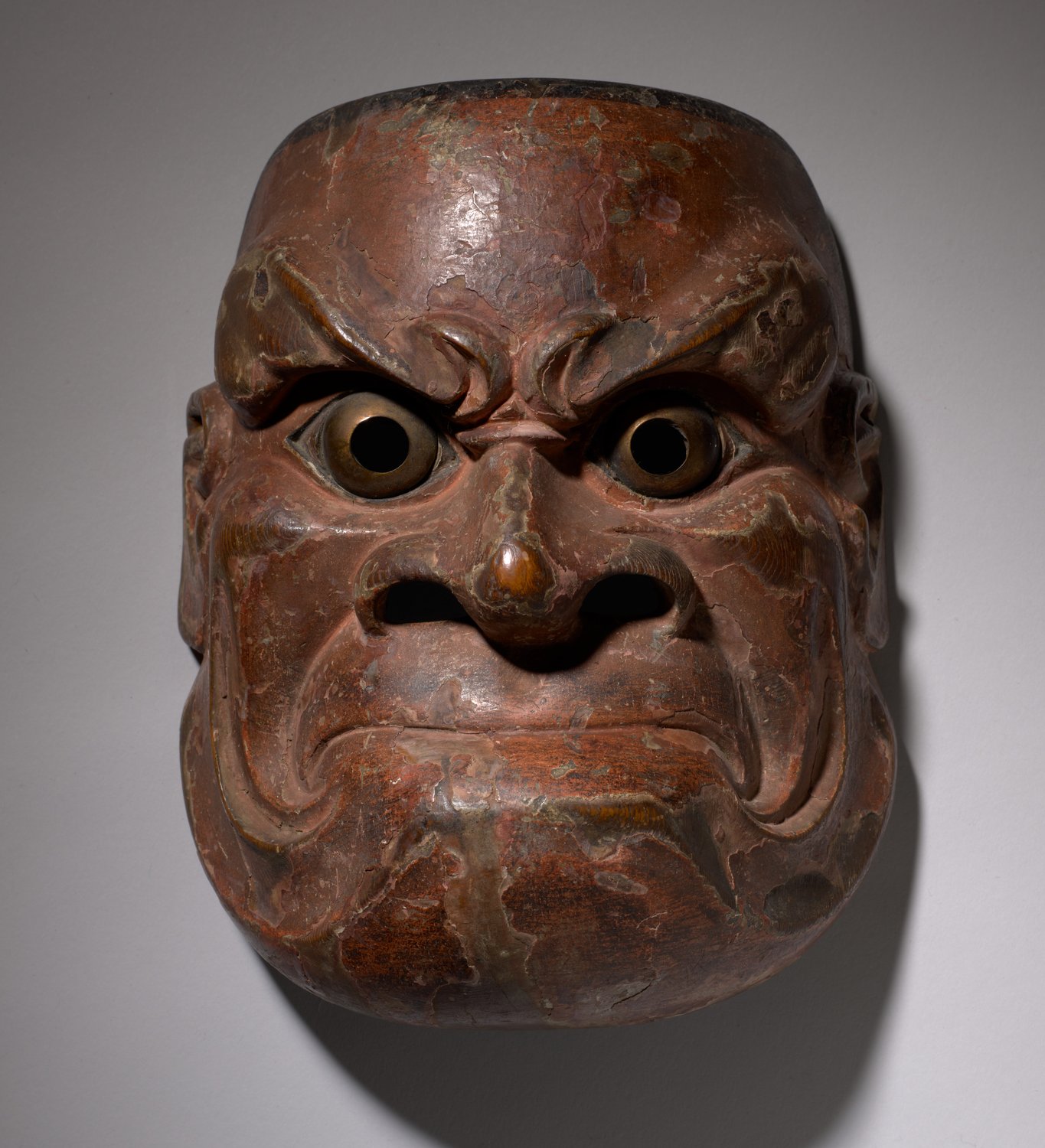 A fierce noh mask with bulging eyes, a heavy brow and a tightly set mouth, carved in the Muromachi period