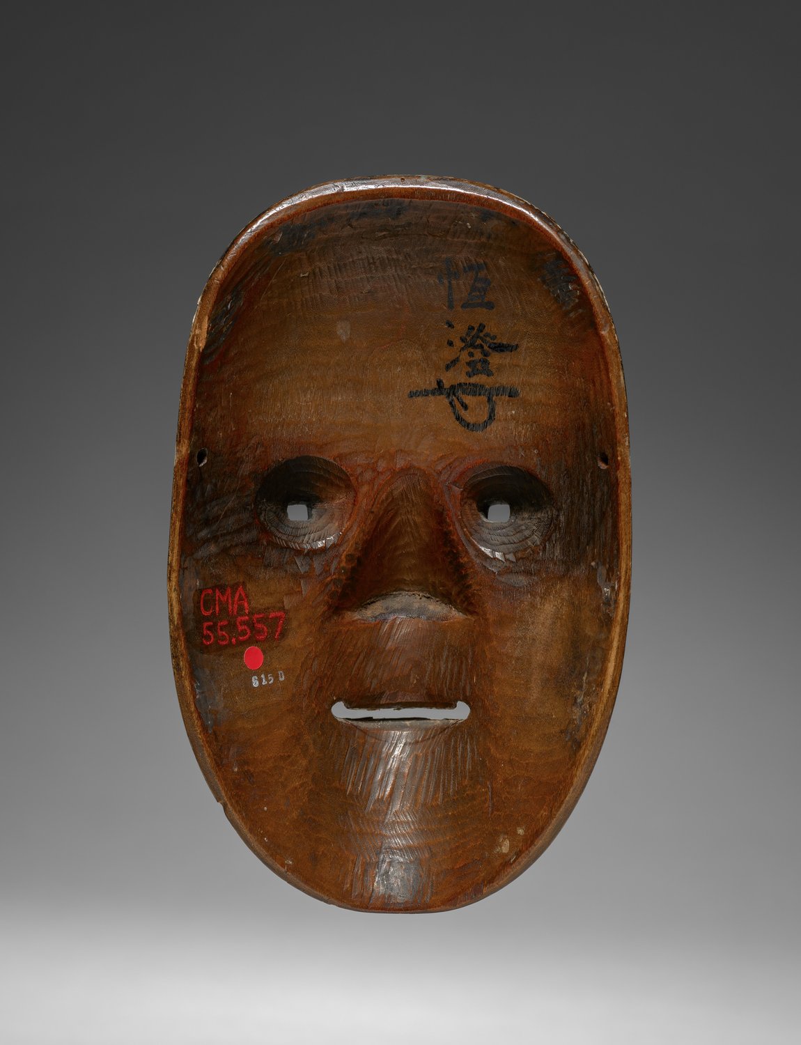 The reverse of a noh mask, showing two eye holes, a mouth opening, tool marks in the wood and brush-written characters near the brow