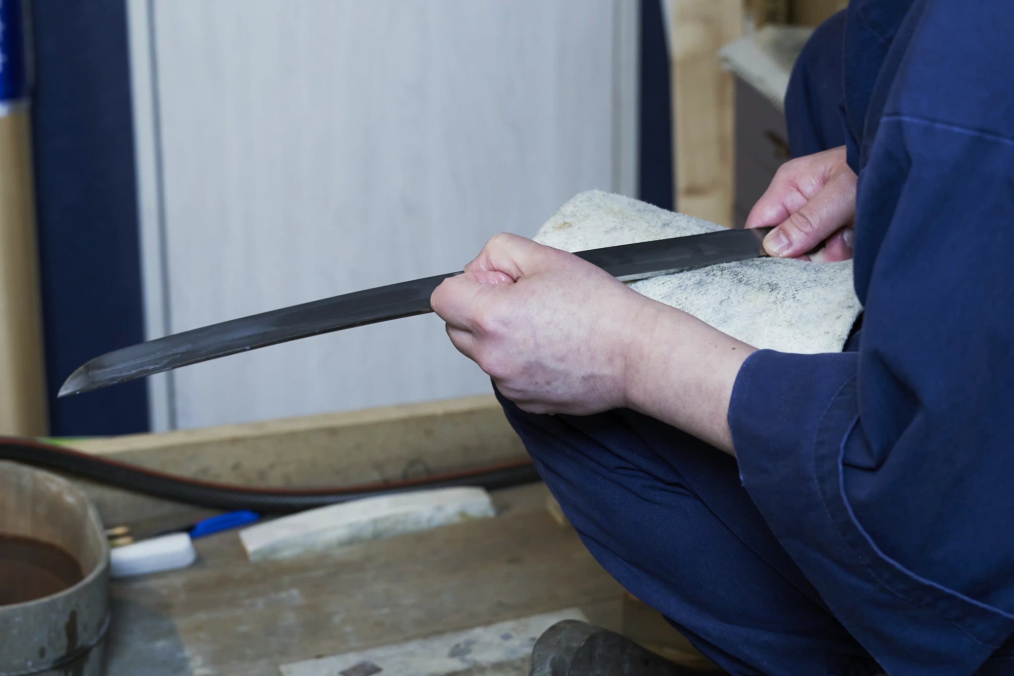 A polisher's hands holding a bare blade, with a sheet of paper in one hand