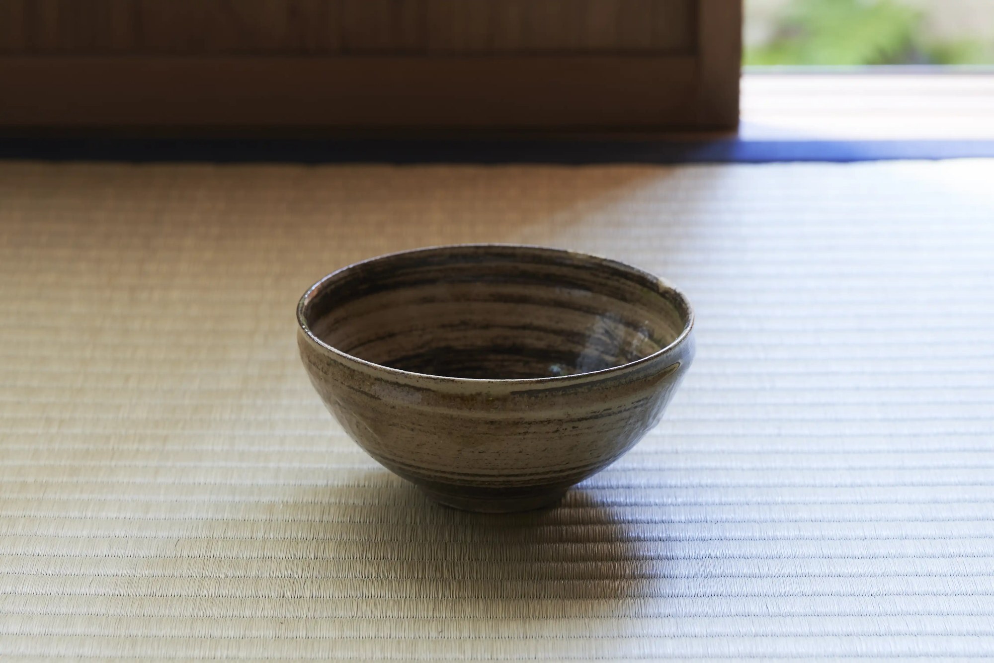A single tea bowl resting on tatami in soft window light