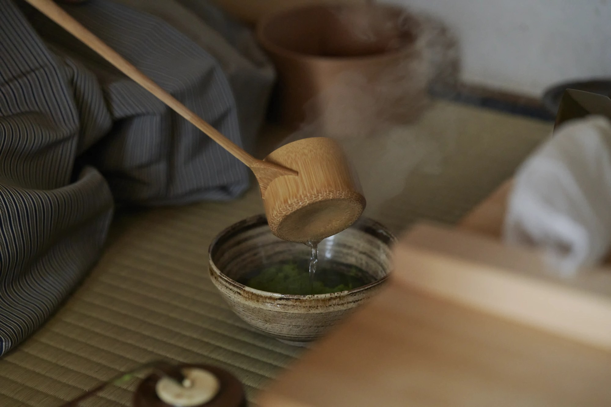 Hot water poured from a bamboo ladle into a tea bowl holding green tea