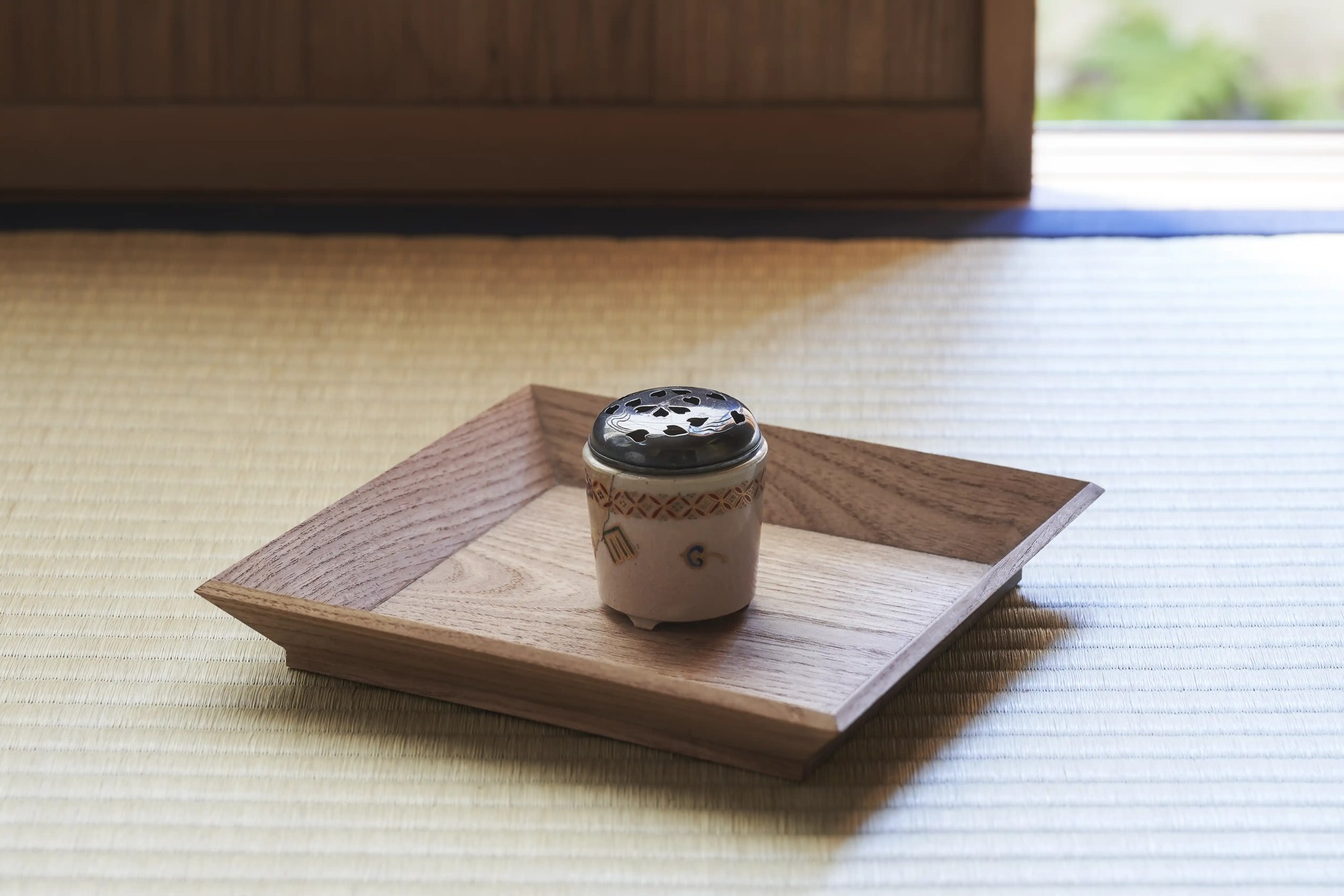 A small lidded ceramic container on a square wooden tray on tatami