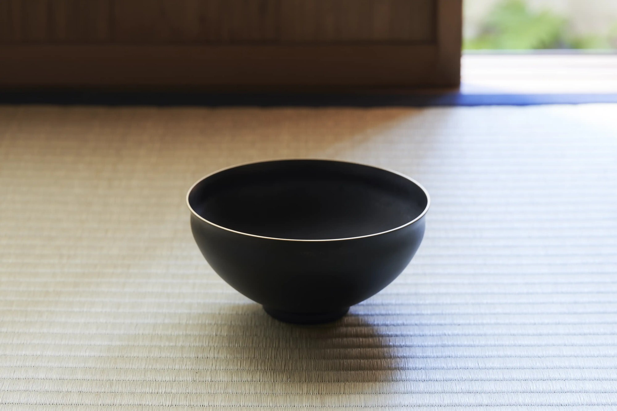 A black tea bowl with a pale rim resting on tatami