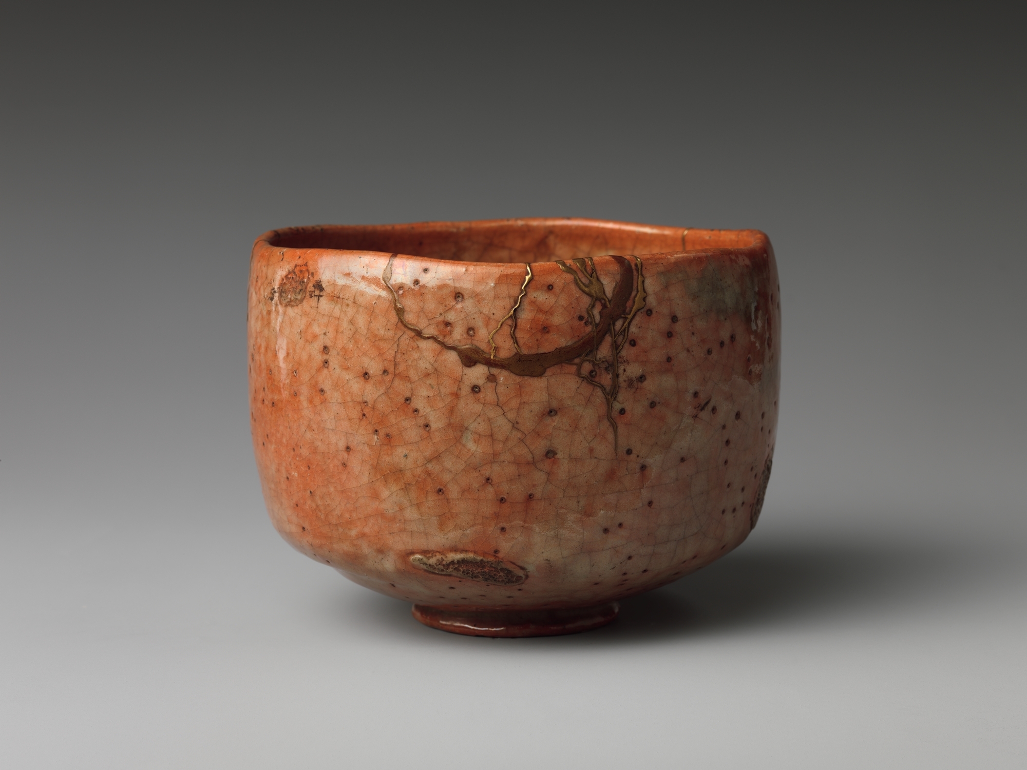 A red raku tea bowl whose medium the Metropolitan Museum of Art lists with gold lacquer repairs