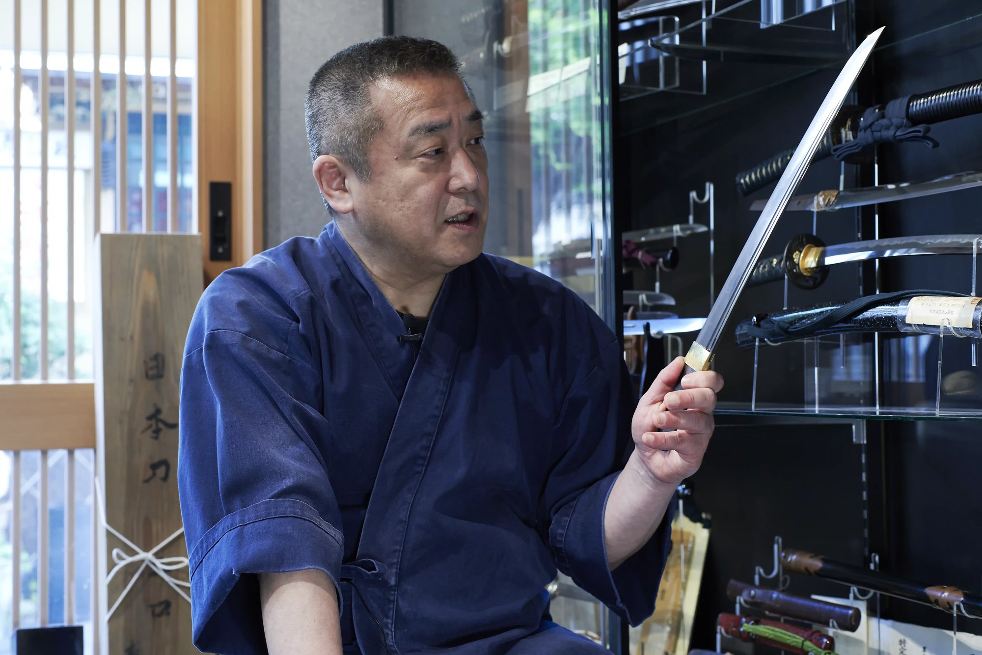 A sword polisher holding up an unmounted blade in front of glass cabinets of swords