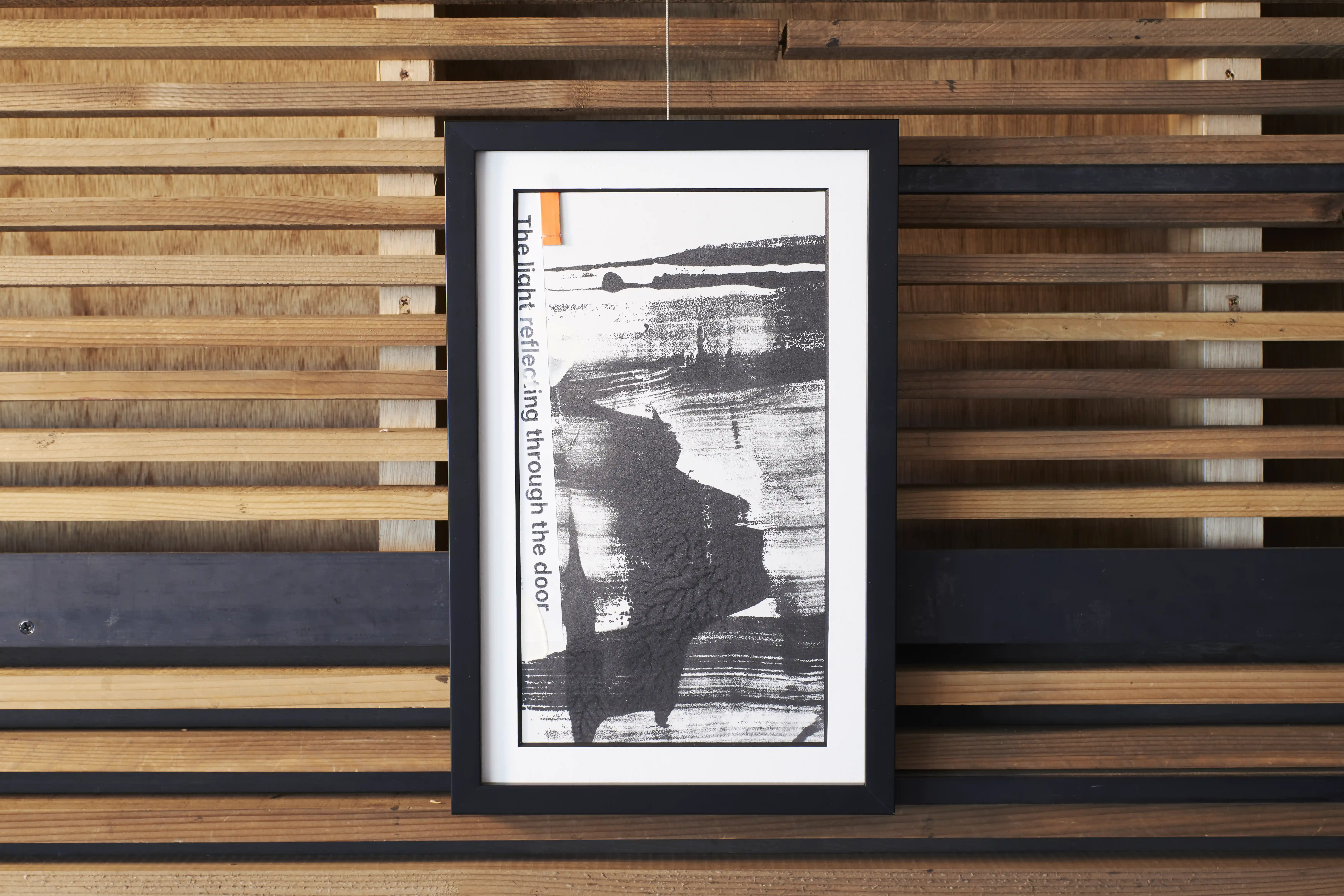 A framed ink work leaning against a slatted wooden wall, the brushstroke running the length of the sheet