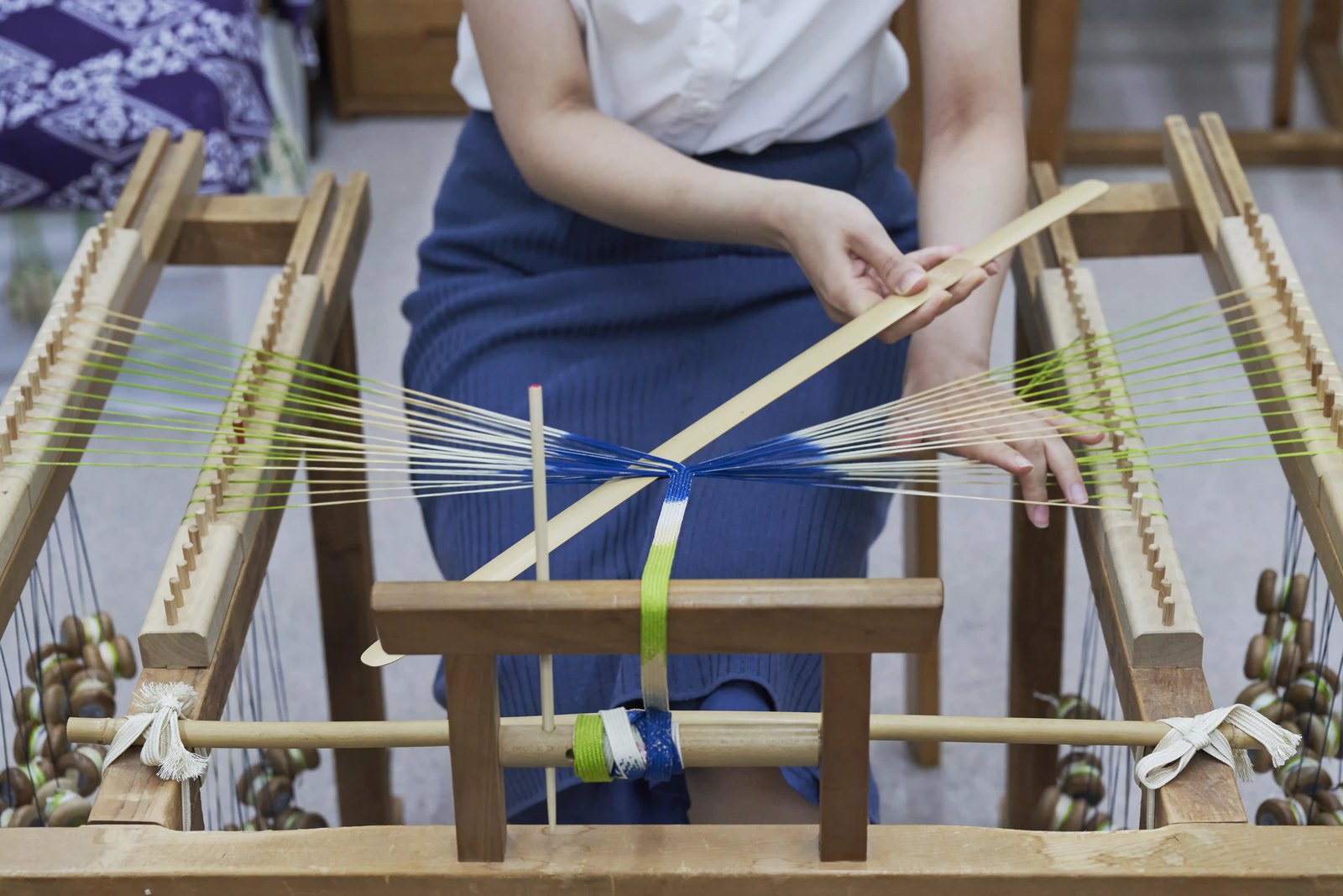 Coloured silk threads strung across a wooden braiding stand, weighted bobbins hanging at the sides
