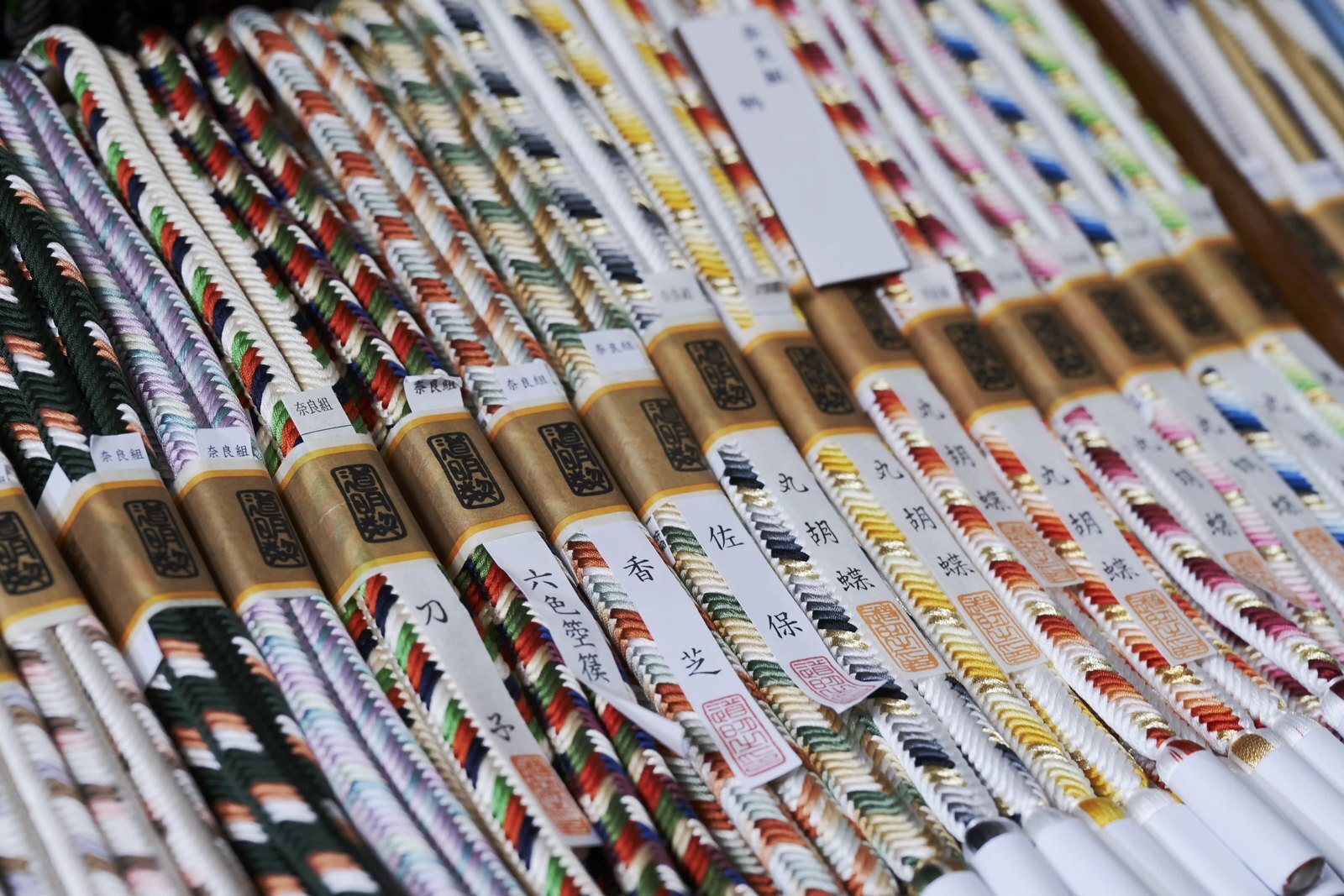 Rows of finished silk obi-jime cords, each with a paper label naming its pattern