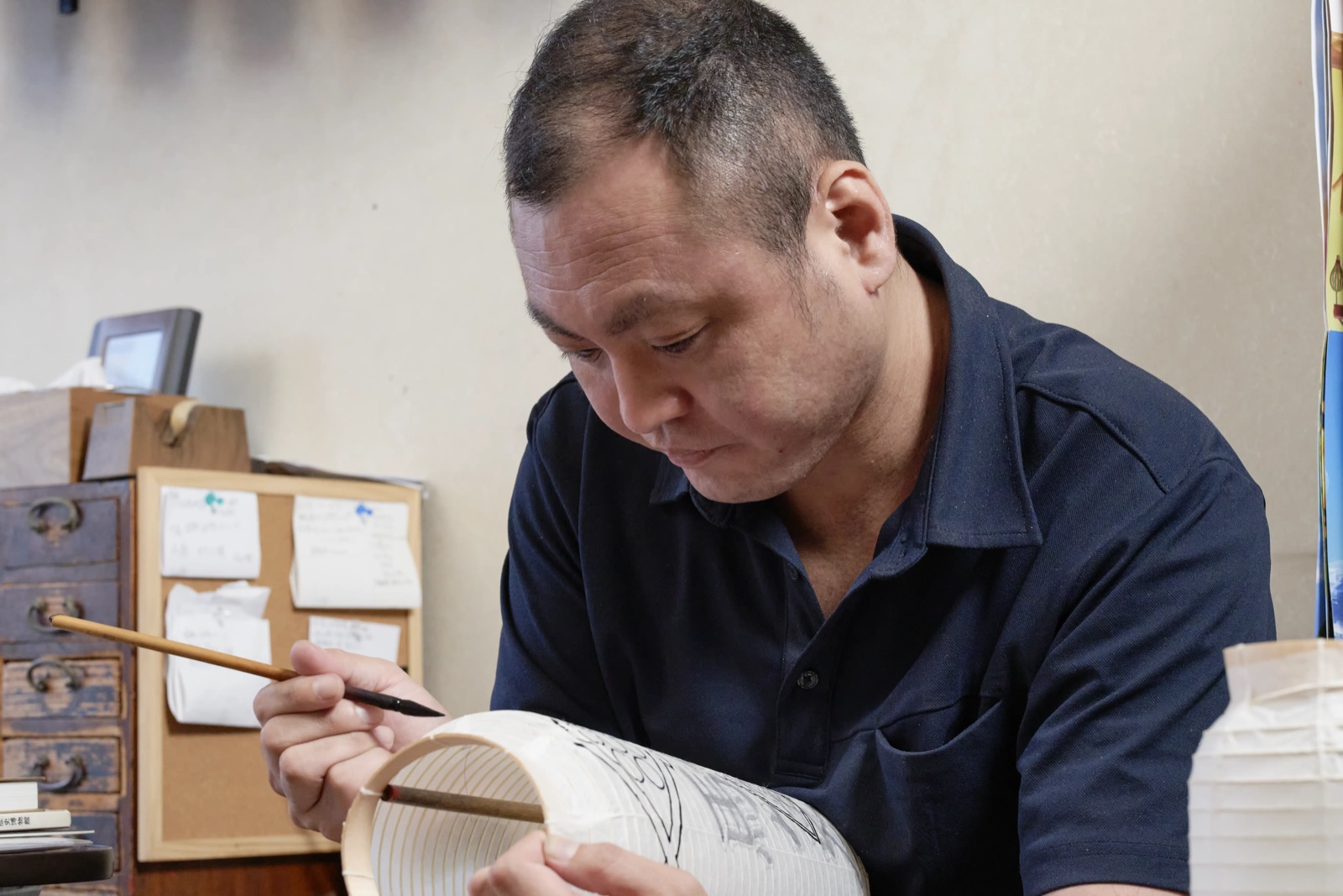 A lantern maker lettering a chochin by hand, the characters drawn straight onto the washi