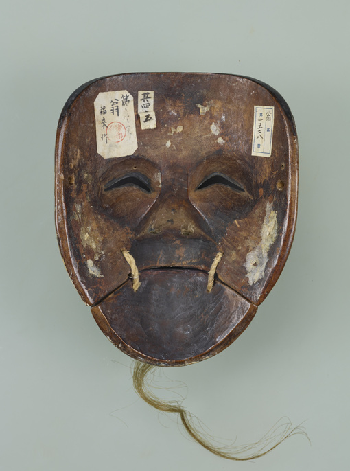 The reverse of a noh mask, old paper labels and a museum accession number pasted onto the hollowed wood