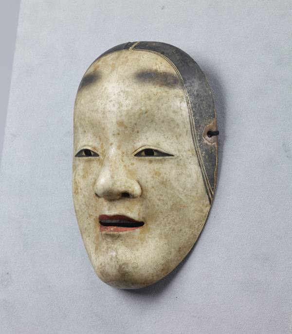 A ko-omote mask lying on a pale cloth-textured ground, seen from slightly above