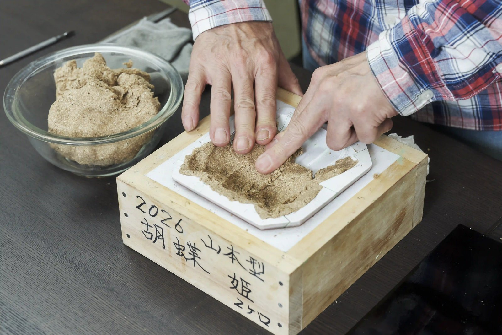 A pressed doll body drying in its wooden mould beside a bowl of the paulownia and paste mixture