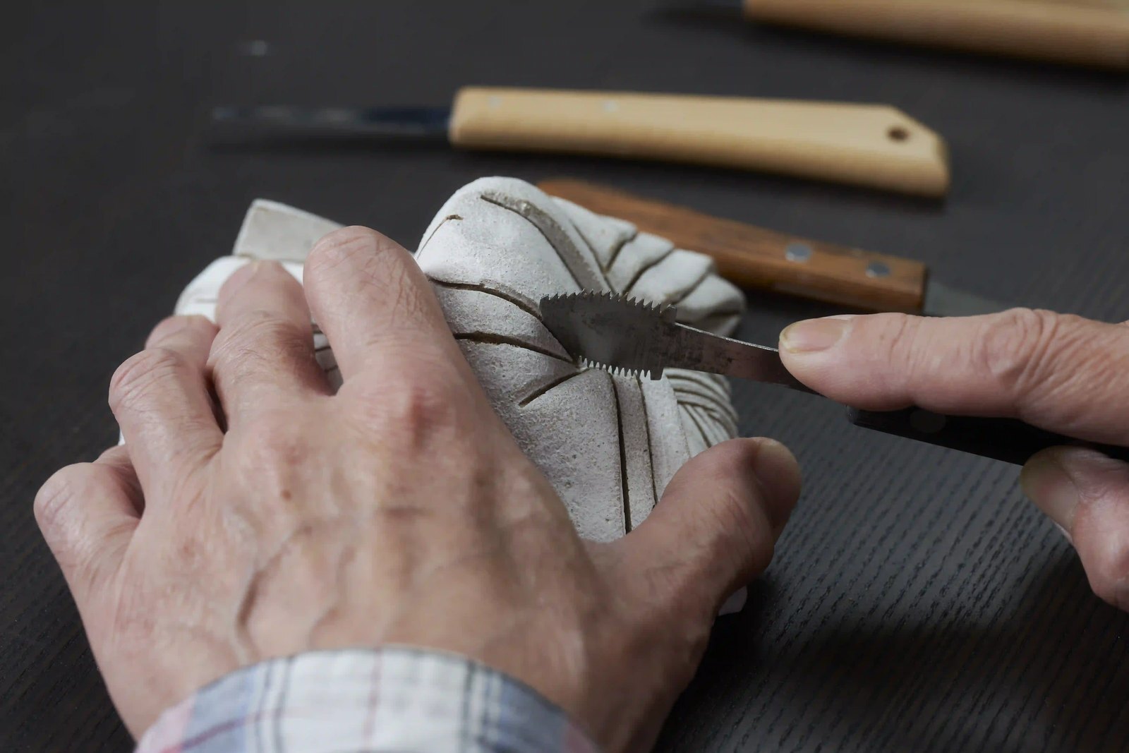 A doll body held in one hand while a blade opens the groove that will hold the tucked fabric