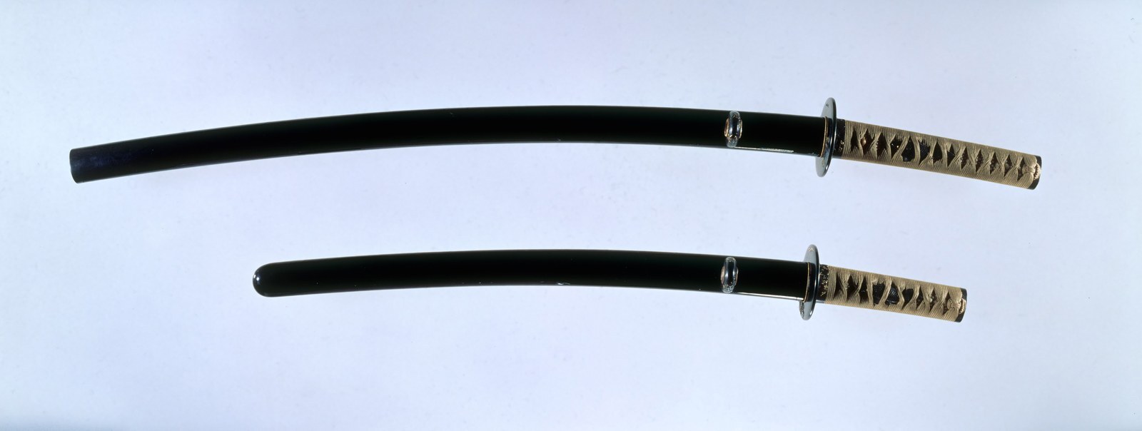 A matched pair of mounted Japanese swords, long and short, lying side by side in their lacquered scabbards