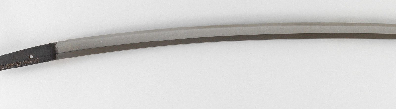 An unmounted Japanese sword blade shown horizontally, its tempered edge running the length of the steel