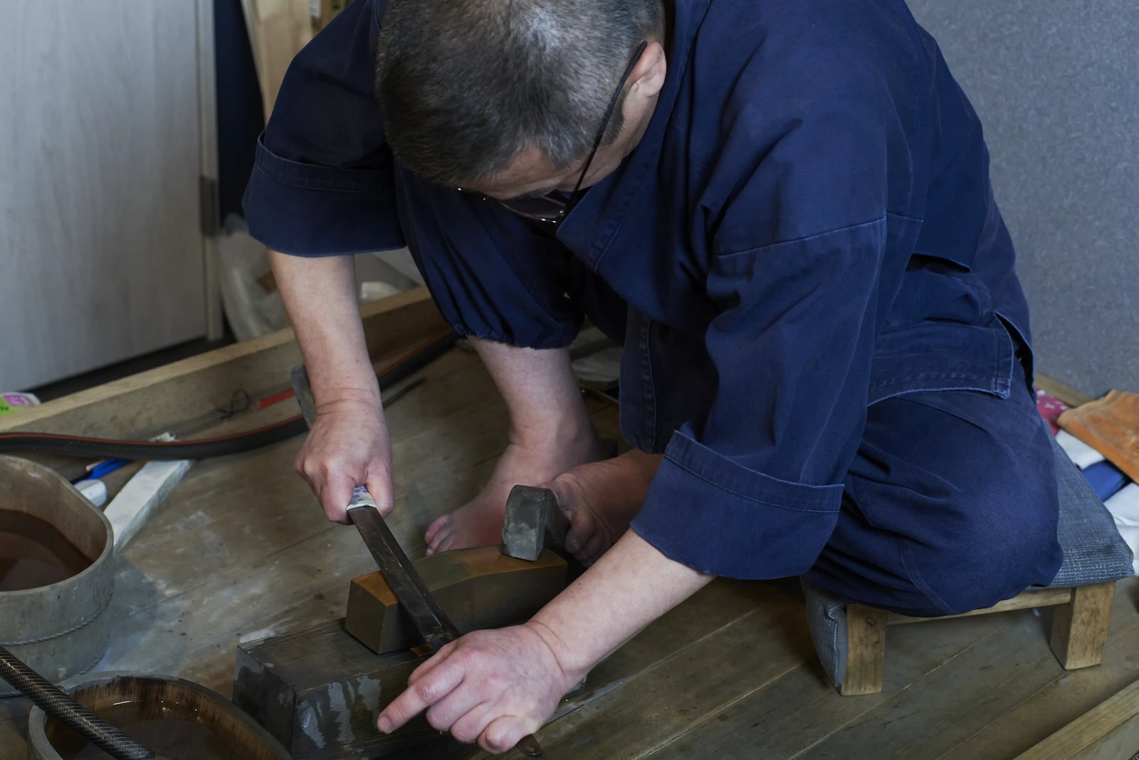 The polisher bent low over his bench, drawing a blade across a wet whetstone set on the wooden block