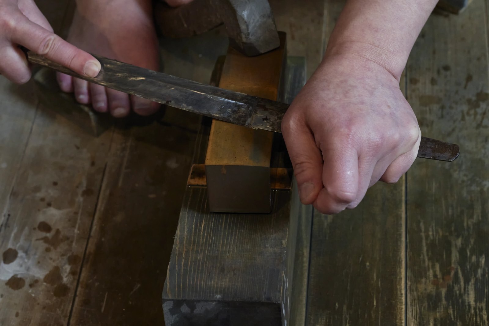 The polisher's hands holding a blade steady against a small stone, working one short section at a time