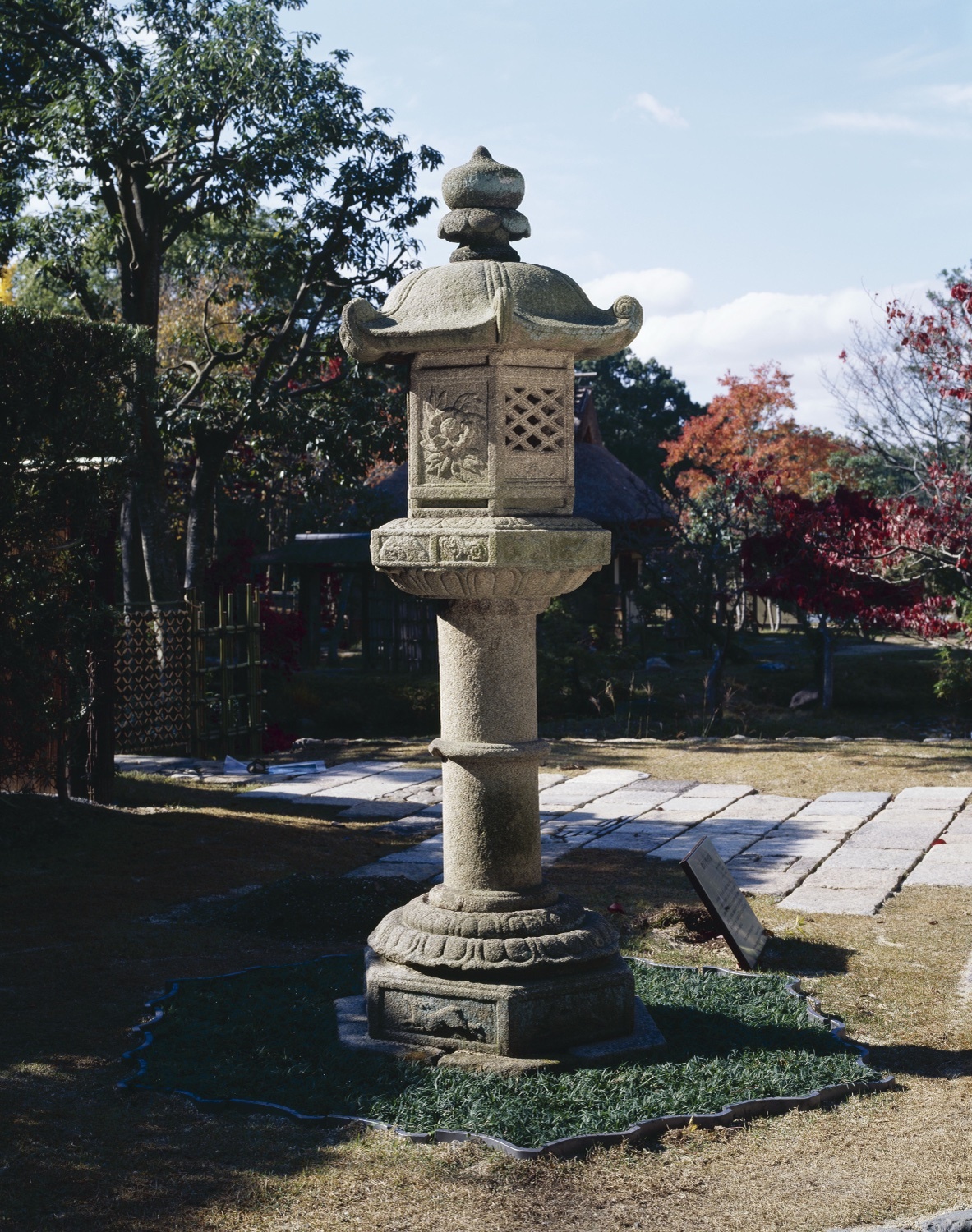 A stone lantern standing outdoors in a garden, its canopy, fire chamber, shaft and base all visible