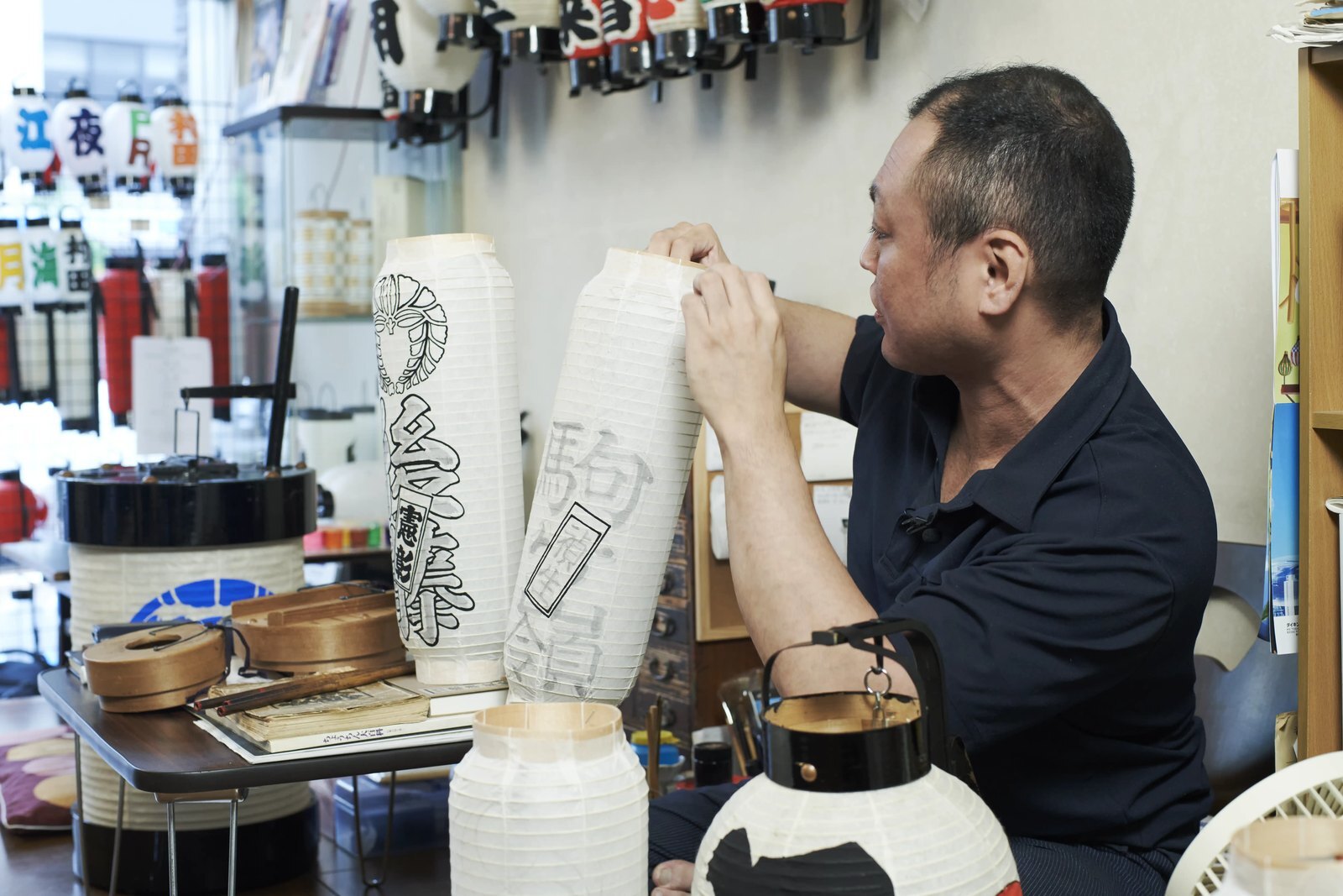 The lantern maker seated at his workbench in the Namidabashi shop, a mounted lantern in front of him