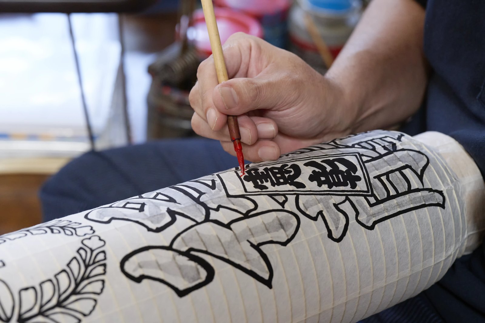 A brush drawing thick outlined characters around the curved face of a paper lantern