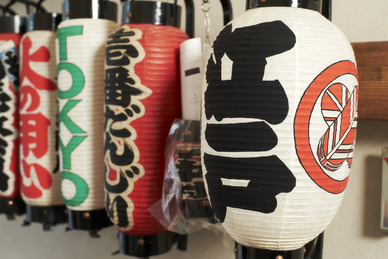 Hand-lettered paper lanterns hanging in a row outside a Tokyo shopfront, bold characters facing the street